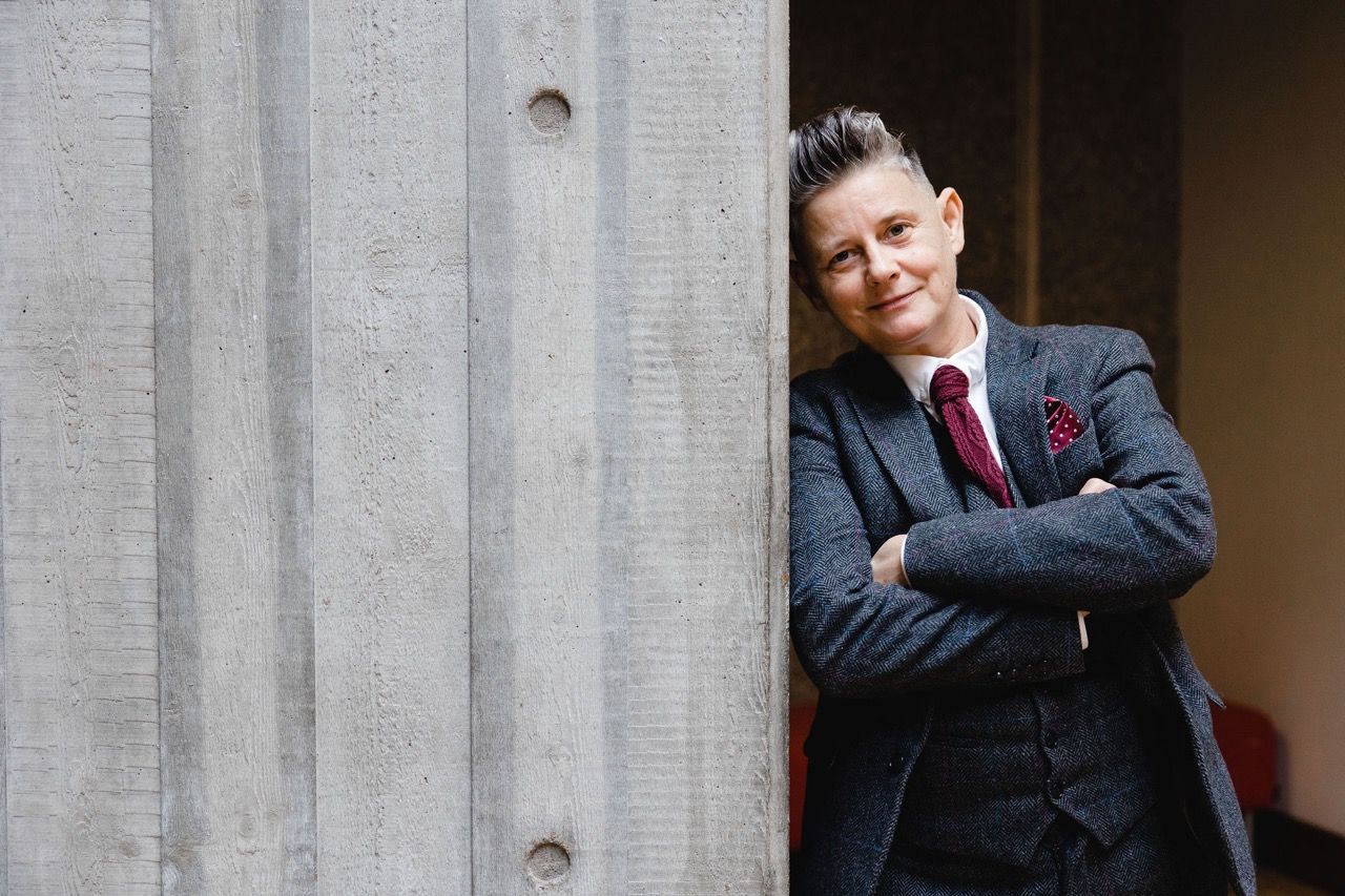 Joelle Taylor beside a against a concrete wall at South Bank Centre, London. Image Christina Davies, Fish2Photo.