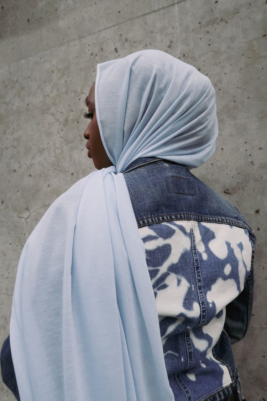 Black woman facing away wearing light blue head scarf over denim jacket, part of the Woke Denim Project by Tiwirayi Ndoro
