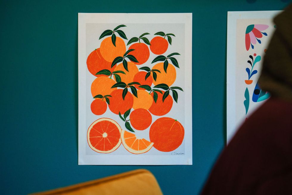 Colourful illustration of oranges by Reyhana Ismail mounted on a teal wall. Image by Rachel Ovenden.