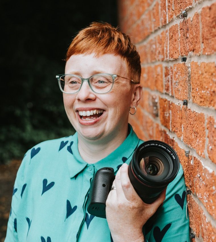 Christina Davies and her camera leaning against a red brick wall