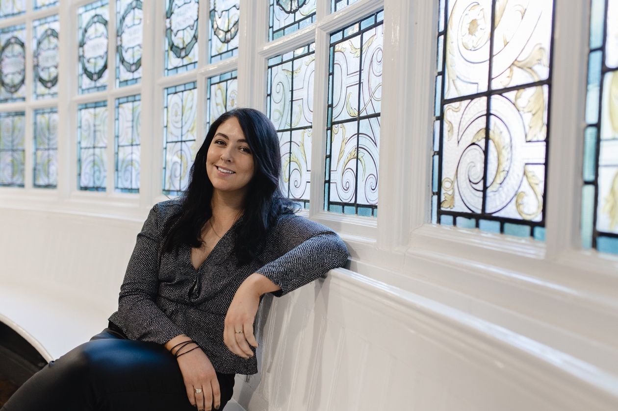 Louiza Cookson Rabouhi seated in front of a decorative stained glass window at The Storey in Lancaster.